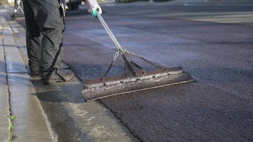 Close-up of worker smoothing fresh asphalt with a tool